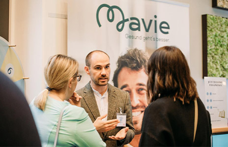 Mann erklärt zwei Frauen etwas bei einem Mavie-Stand (Foto)