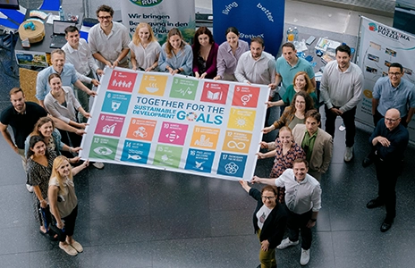 A group of around 20 people holding a poster with SDG goals.
