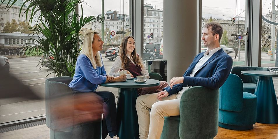 The UNIQA Tower offers ample space for exchange among employees. Pictured: two women and one man sitting comfortably in Café Aioli on the ground floor.
