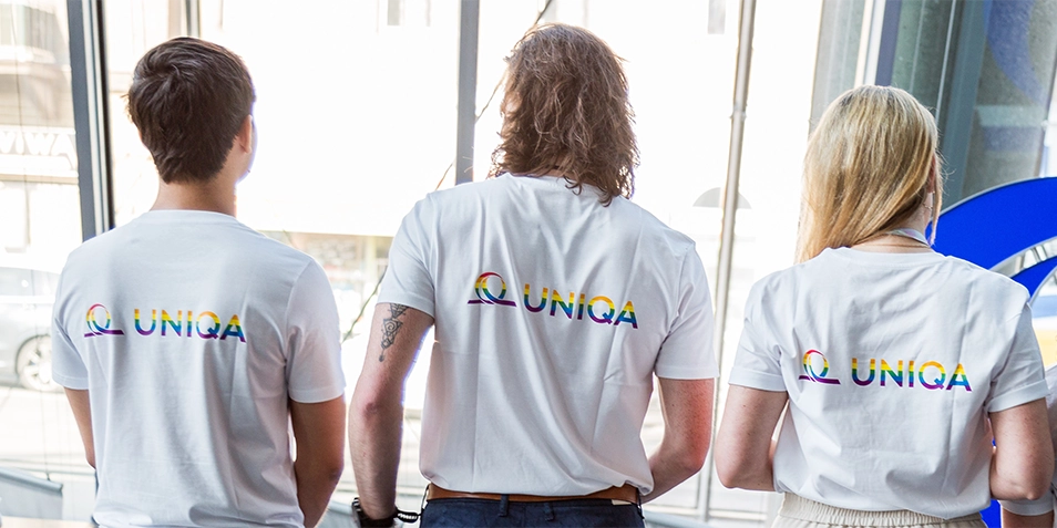 Rückansicht von drei jungen Menschen mit T-Shirts mit UNIQA-Logo in Regenbogenfarben.